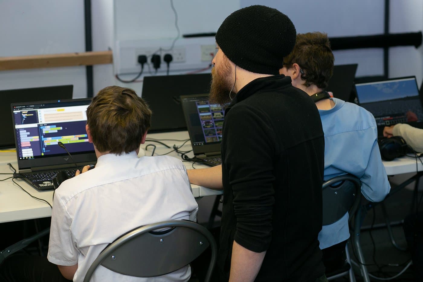 A mentor helping young coders at a Player Ready coding club session, guiding them through Minecraft modding on laptops