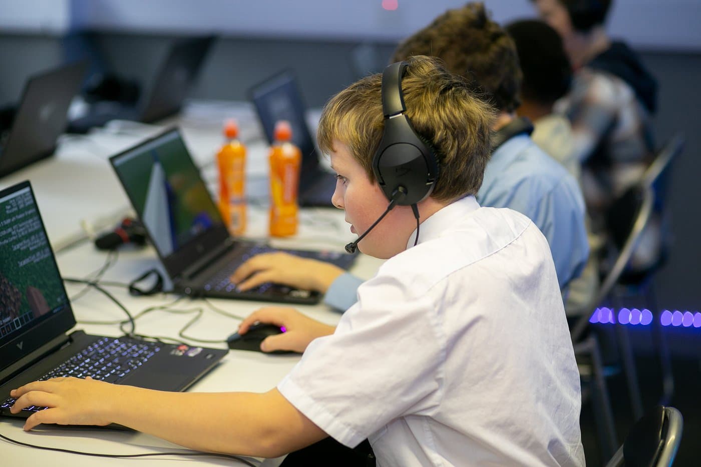 Real kids at a Player Ready coding club session with headsets and laptops, learning Minecraft modding